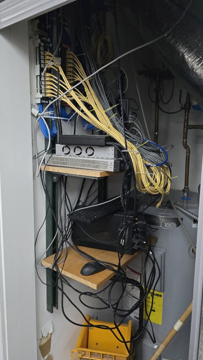 Disorganized office network closet with cabling and equipment needing low-voltage infrastructure cleanup