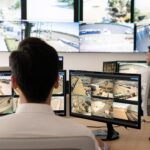 Professional security command center with operators monitoring multiple live CCTV camera feeds on large video walls and desks — commercial surveillance control room by Apollo Technology & Cabling